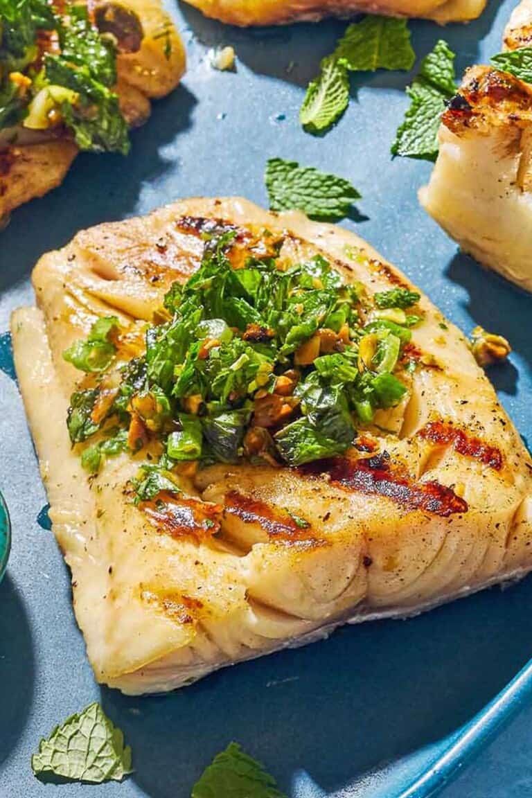 A close up of a grilled cod filet topped with a pistachio-herb salsa.