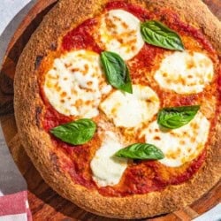 An overhead photo of a pizza with a whole wheat pizza crust on a wooden serving platter with a kitchen towel.