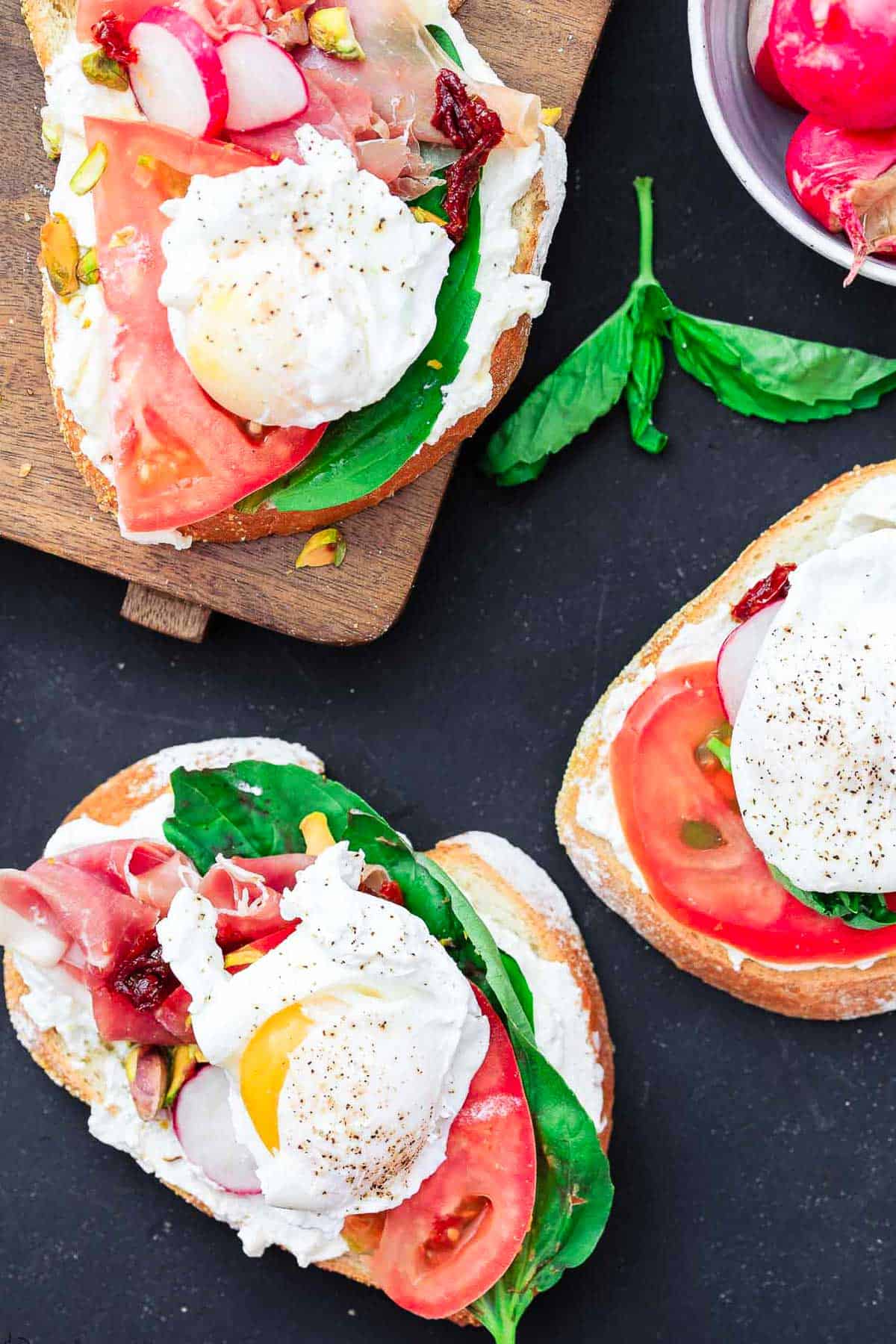 Three open faced sandwiches. One is on a cutting board and two are on the counter.