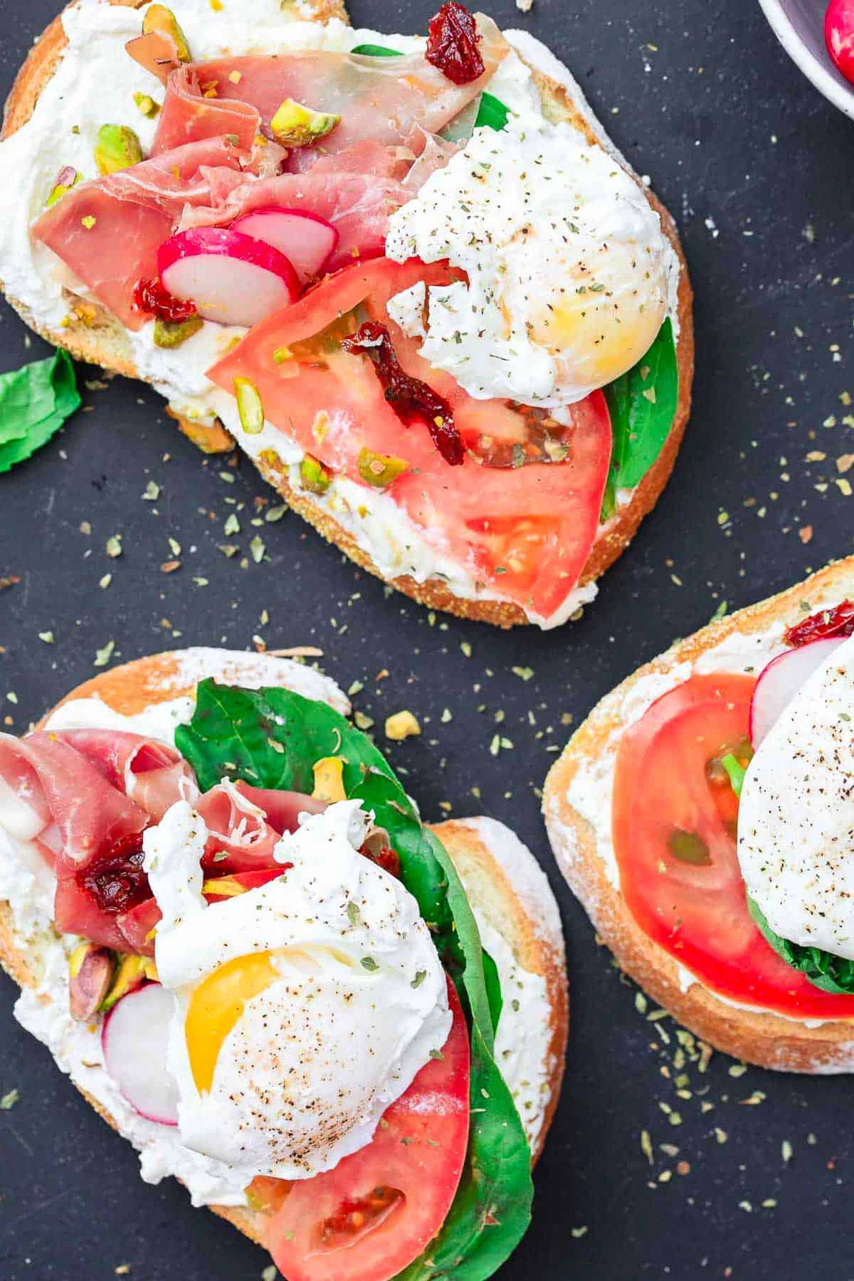 Three open faced sandwiches, showing the prosciutto, basil, tomato, radish, poached eggs, and pistachios.