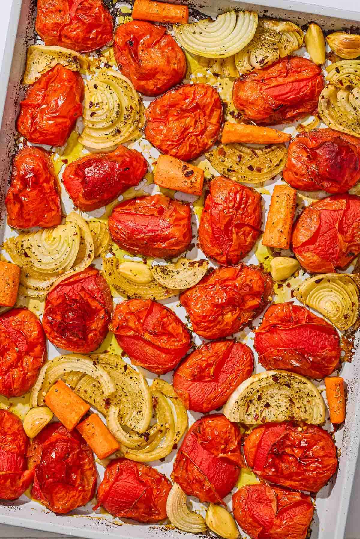 An overhead photo of roasted onions, tomatoes, carrots and garlic on a baking sheet.