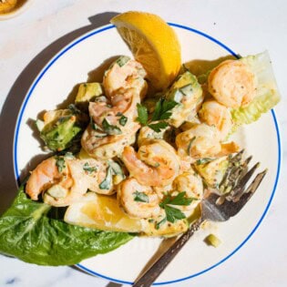 Overhead shot of a serving of shrimp salad on a plate with a lemon wedge on the side.