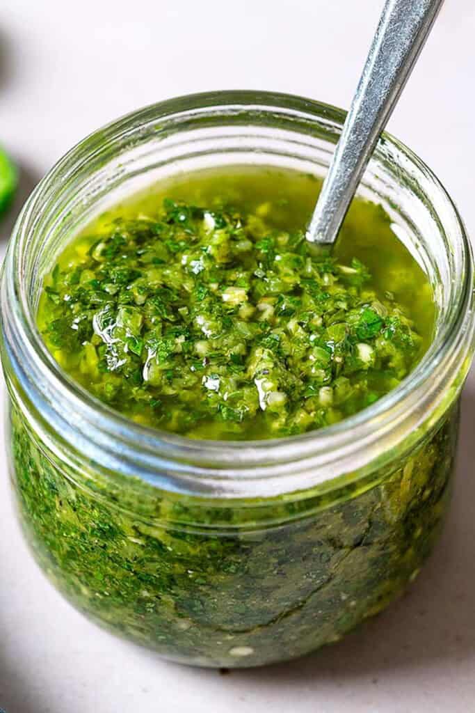 A close up of zhoug in a jar with a spoon.