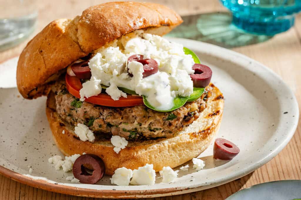 A close up of a greek style lamb burger on a plate.