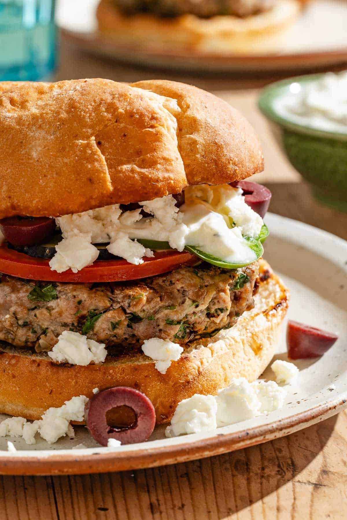 A close up of a greek style lamb burger on a plate.