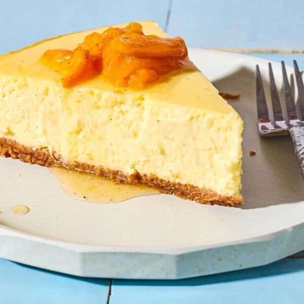 A close up of a slice of the greek yogurt cheesecake topped with the apricot, vanilla and honey compote on a plate with a fork.