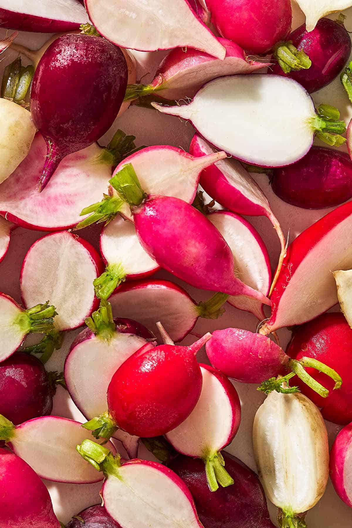 A close up of halved radishes in many different colors — white, pink, and red.