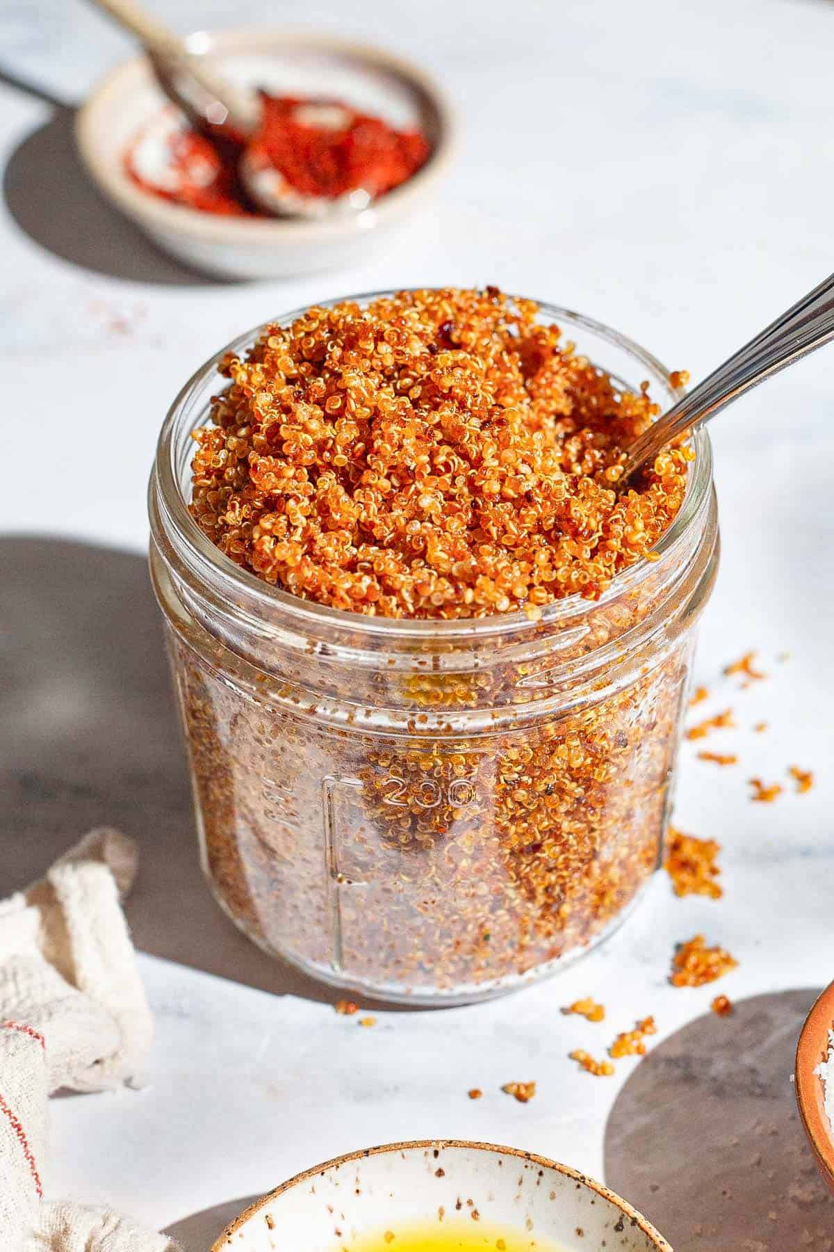 A close up of crispy quinoa in a jar with a spoon.