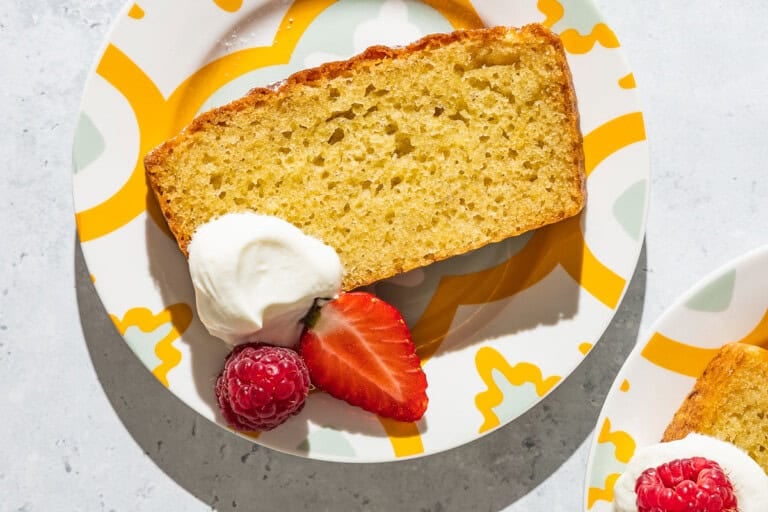 A close up of a slice of yogurt cake on a plate with a dollop of greek yogurt, a strawberry and a raspberry.
