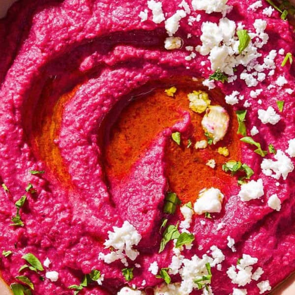 A close up of beet hummus in a bowl topped with olive oil, feta cheese and parsley.
