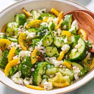 Smashed cucumber salad in a serving bowl with wooden serving utensils.