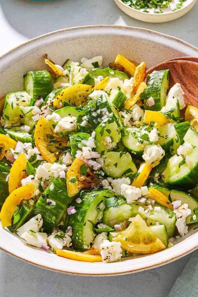 Smashed cucumber salad in a serving bowl with wooden serving utensils.