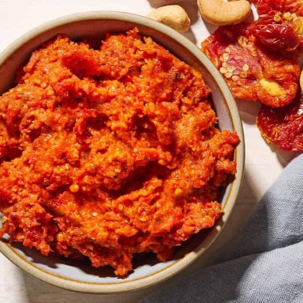 An overhead photo of sun dried tomato pesto in a bowl. Next to this is a cloth napkin, and some cashews and sun dried tomatoes.