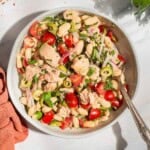 An overhead photo of tuna white bean salad in a serving bowl with a spoon. Next to this is a cloth napkin, sprigs of basil and parsley, and bowls of aleppo pepper and kosher salt.