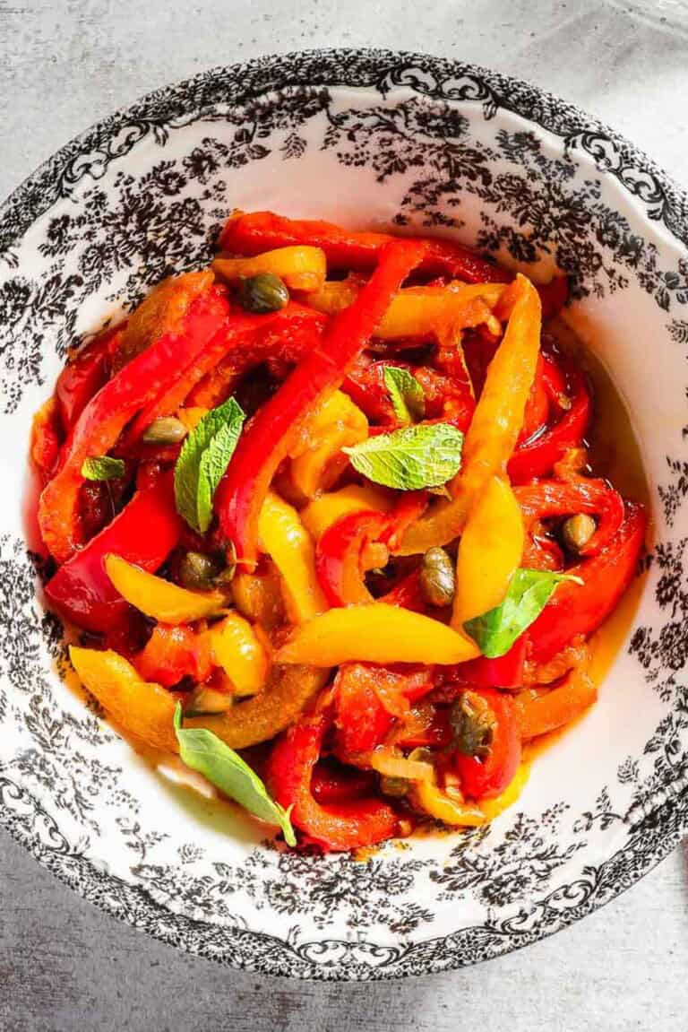 An overhead photo of peperonata in a bowl. Next to this is a glass and slices of grilled bread.