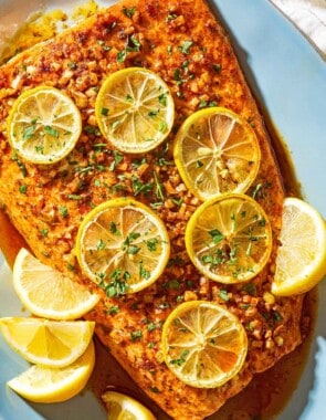 An overhead photo of a lemon garlic salmon fillet topped with lemon wheels and parsley on a serving platter with lemon wedges.