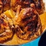 A close up of 4 roasted cornish hens in a large skillet with lemon wedges.
