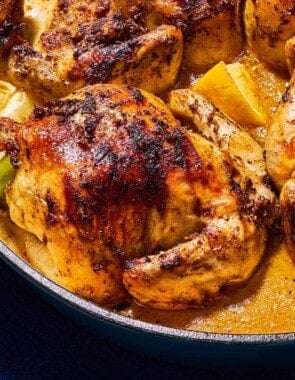 A close up of 4 roasted cornish hens in a large skillet with lemon wedges.
