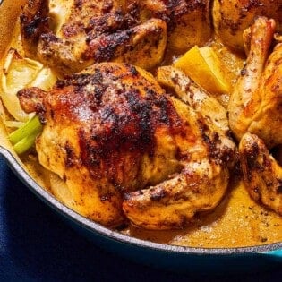 A close up of 4 roasted cornish hens in a large skillet with lemon wedges.