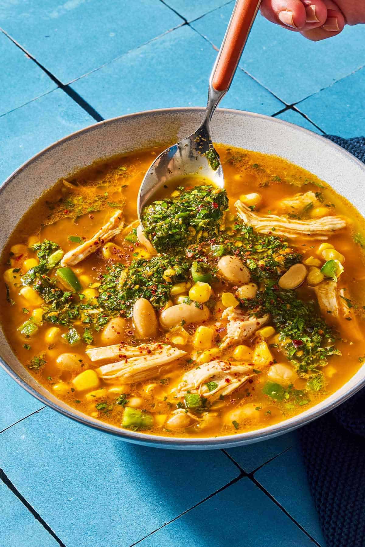 A close up of white chicken chili in a bowl being topped with chermoula with a spoon.