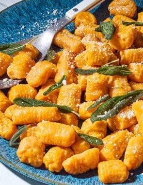 A close up of sweet potato gnocchi and sauce topped with fresh sage on a serving platter with a spoon.