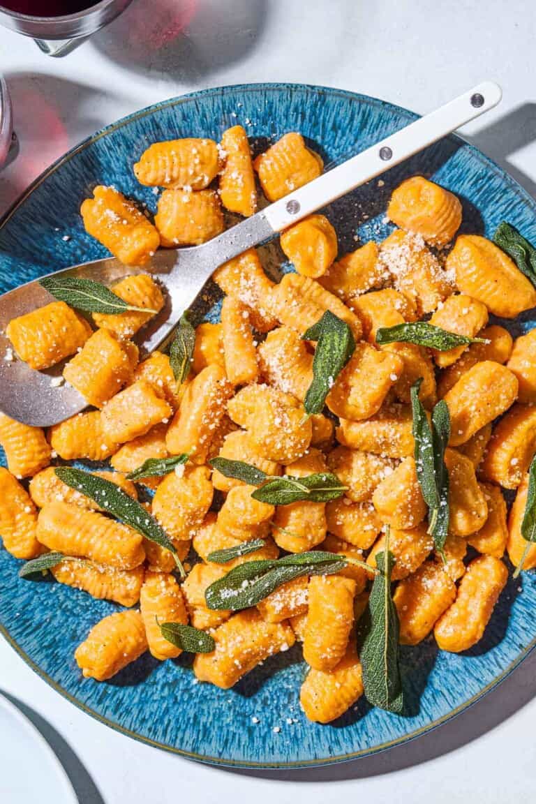 Sweet potato gnocchi and sauce topped with fresh sage on a serving platter with a serving spoon spoon.