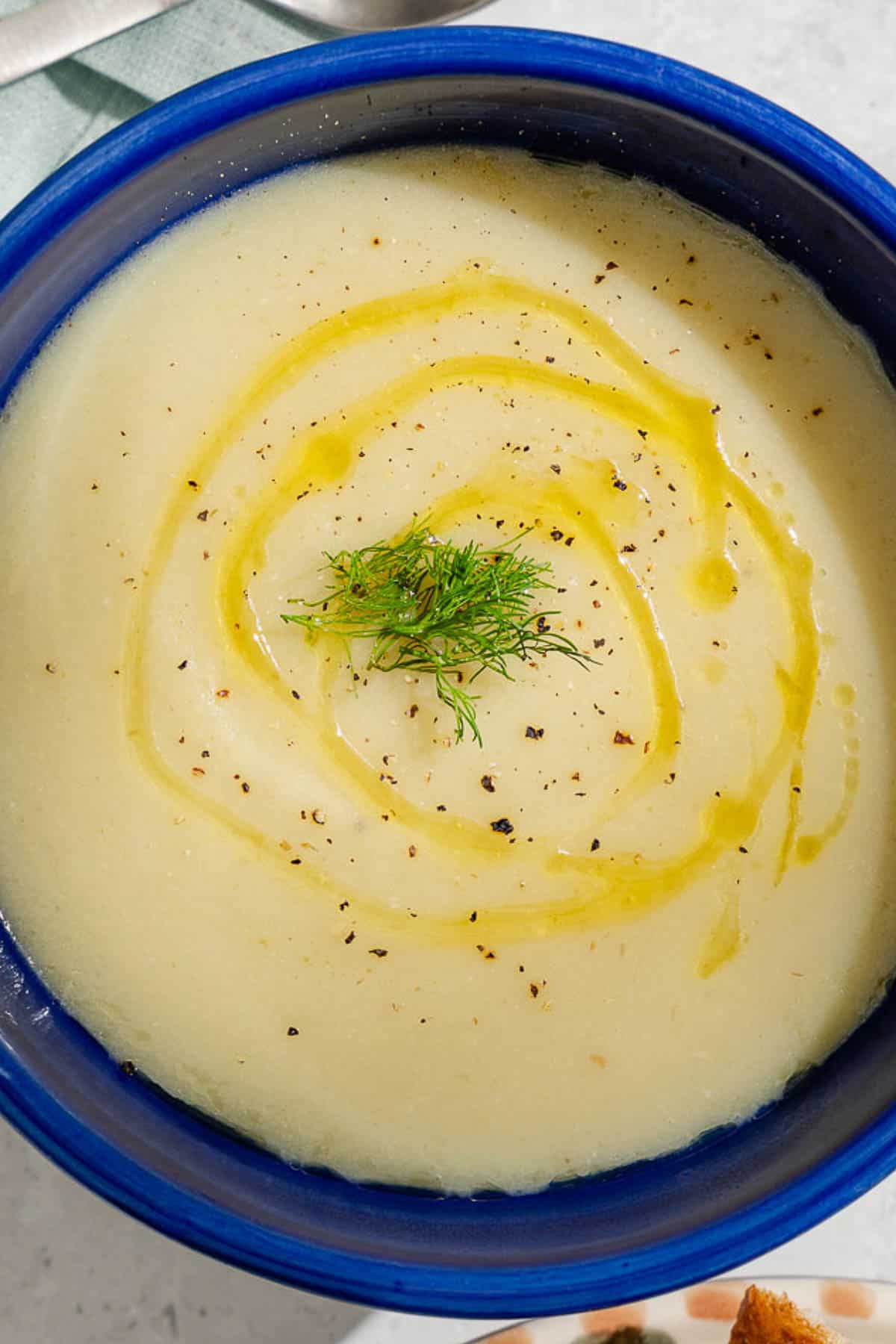 An overhead photo of a bowl of fennel soup topped with a drizzle of olive oil and fennel fronds.
