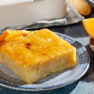 A close up of a piece of portokalopita greek orange cake on a plate next to another plate with orange wedges.