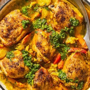 A close up of creamy saffron chicken with mascarpone and lemony cilantro dressing in a skillet with a serving spoon.