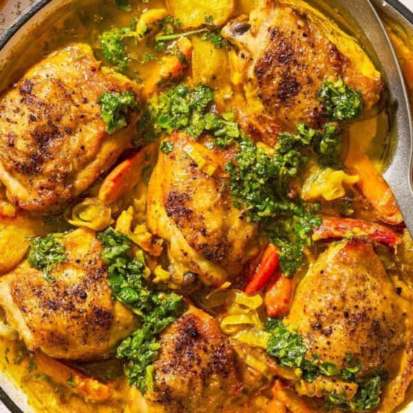 A close up of creamy saffron chicken with mascarpone and lemony cilantro dressing in a skillet with a serving spoon.