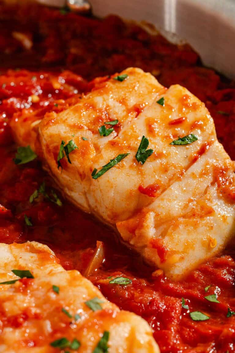A close up of a tomato sauce poached cod fillet.