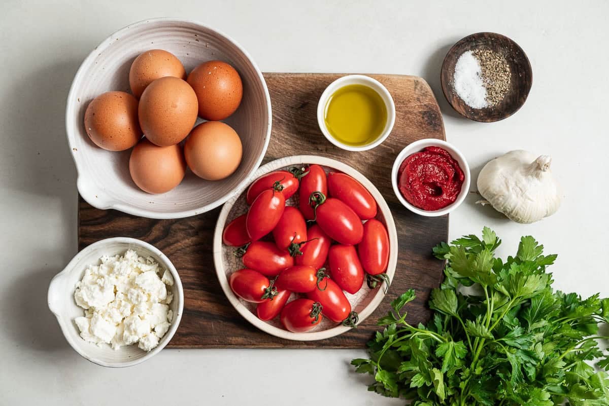 Ingredients for strapastada greek tomato scrambled eggs including eggs, grape tomatoes, salt, black pepper, garlic, tomato paste, water, feta and parsley.