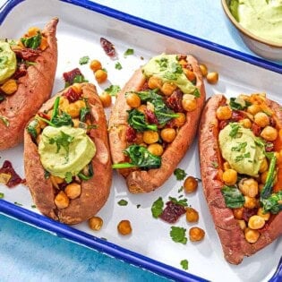 A close up of 4 stuffed sweet potatoes with avocado crema on a platter next to a bowl of avocado crema.