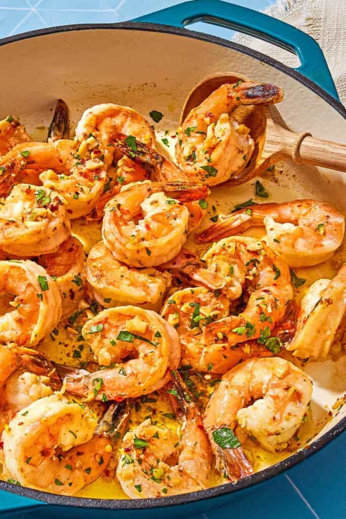 A close up of shrimp scampi in a skillet with a wooden spoon.