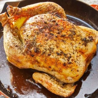A roasted whole chicken rubbed in italian seasoning in a skillet.