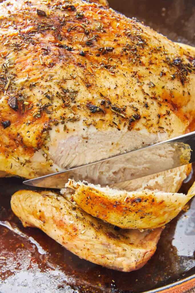 A roasted whole chicken being sliced with a knife.