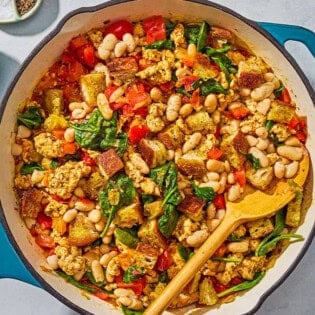 The ground turkey recipe in a skillet with a wooden spoon next to a stack of two plates a bowl with salt and black pepper, and a small bowl of grated parmesan cheese.