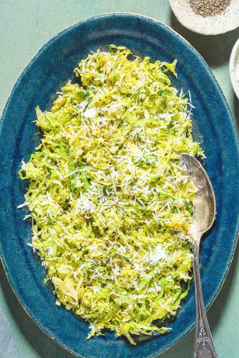 Cabbage cacio e pepe on a platter with a serving spoon next to a bowl of black pepper.