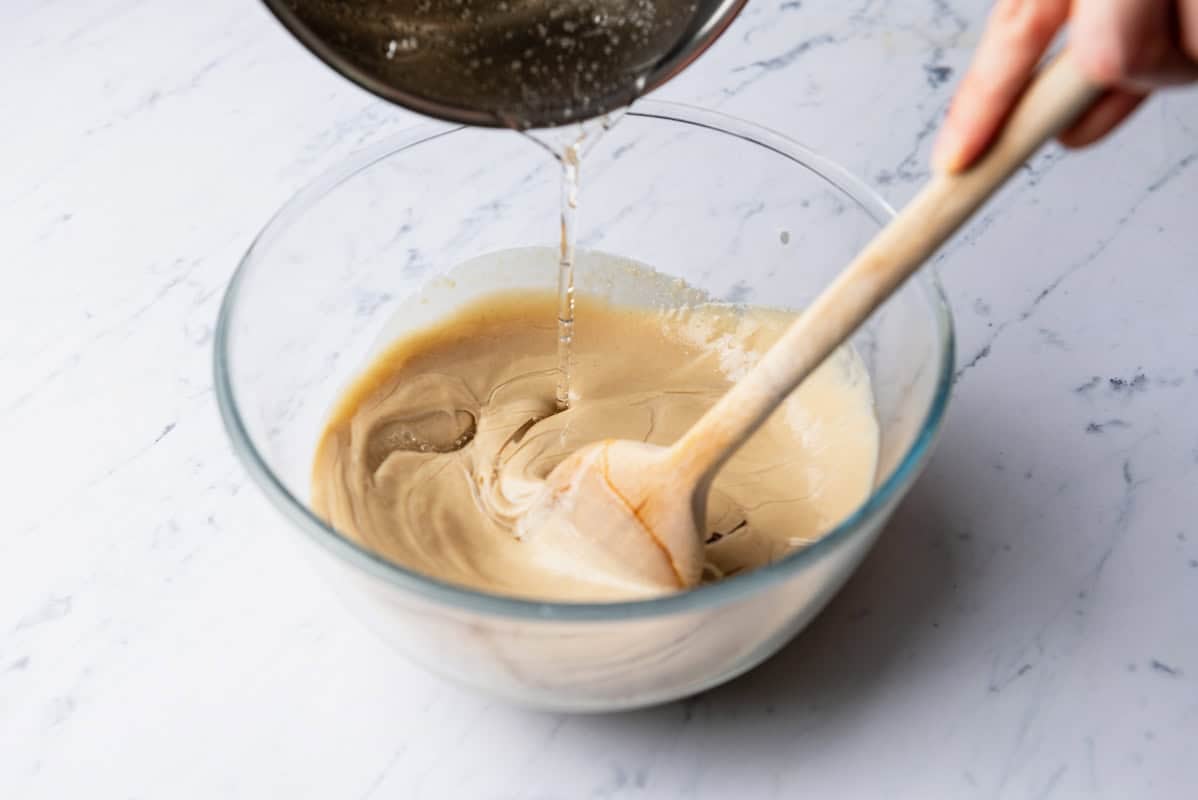 The hot sugar syrup being poured into the rest of the halva mixture while it's being stirred with a wooden spoon.