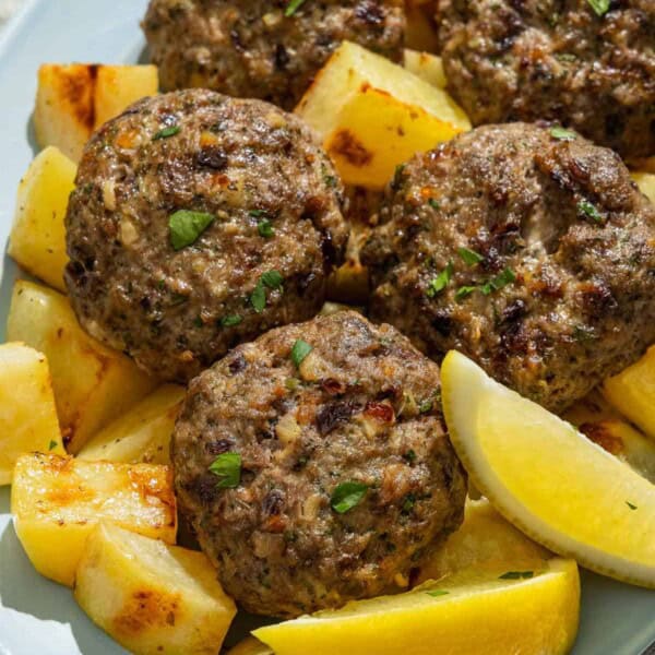 Biftekia with lemon potatoes and lemon wedges on a platter.