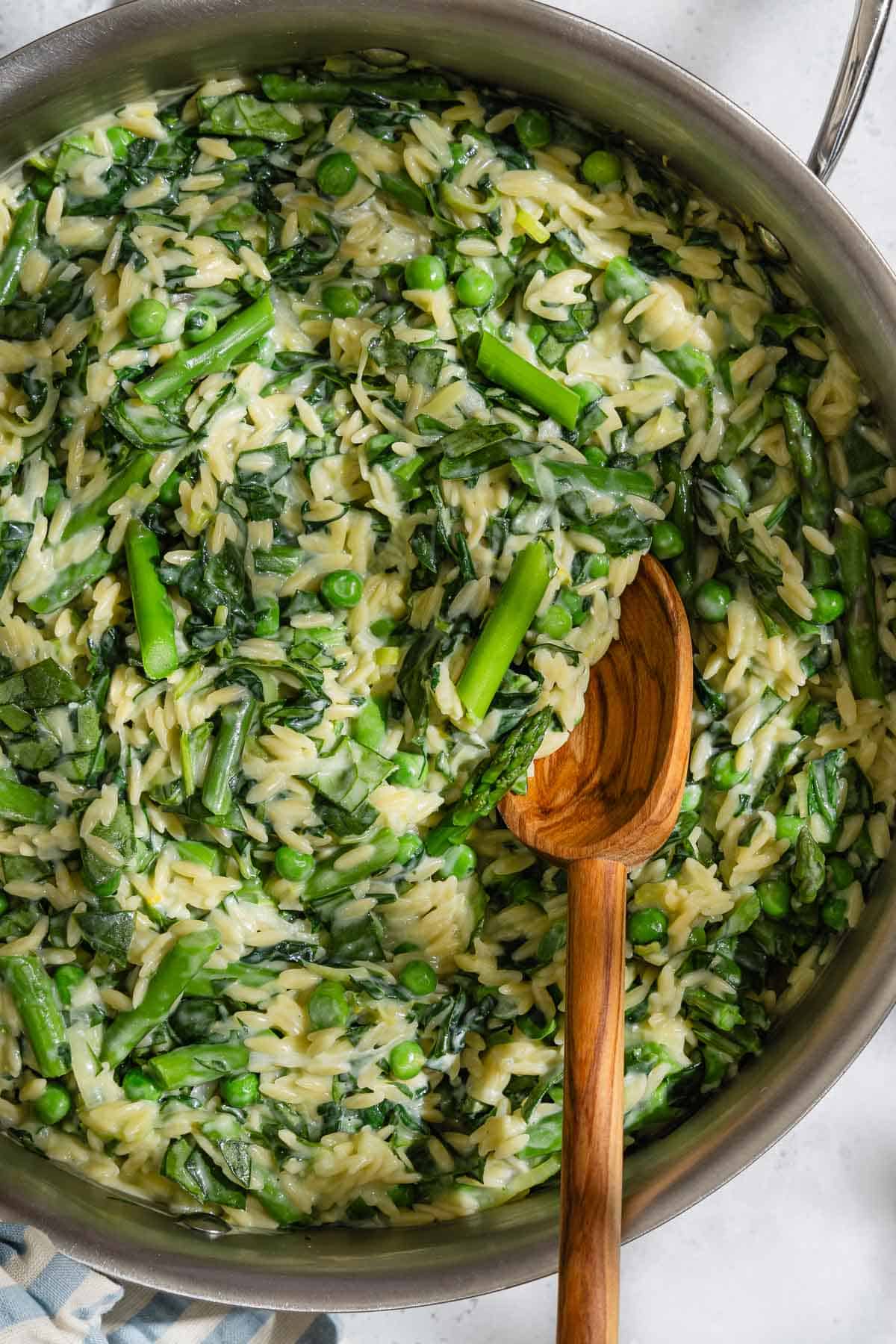 Orzo risotto in a skillet with a wooden spoon.
