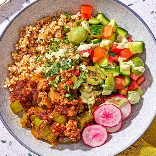 A Mediterranean beef bowl next to a fork and a cloth napkin.