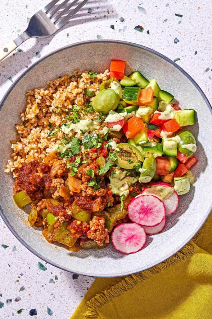 A Mediterranean beef bowl next to a fork and a cloth napkin.