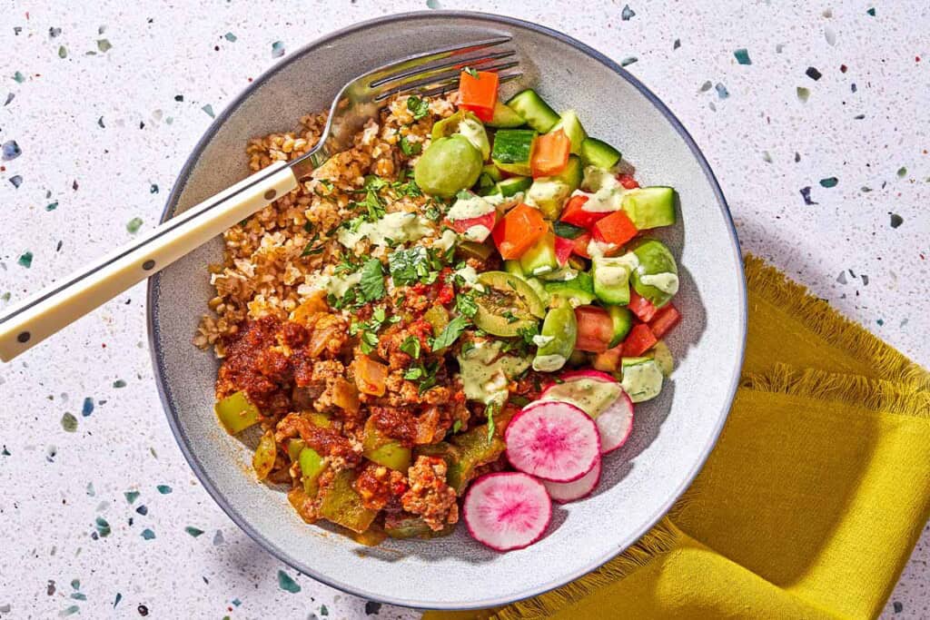 A Mediterranean beef bowl with a fork next to a cloth napkin.