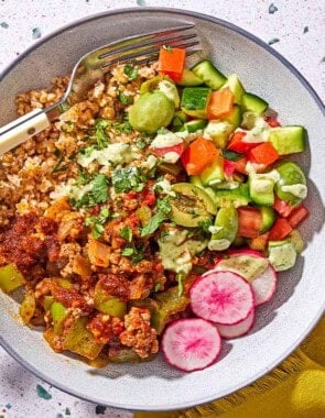 A Mediterranean beef bowl with a fork next to a cloth napkin.