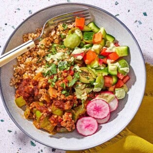 A Mediterranean beef bowl with a fork next to a cloth napkin.