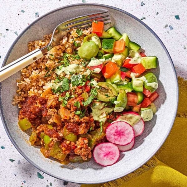 A Mediterranean beef bowl with a fork next to a cloth napkin.