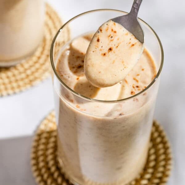A spoonful of the date shake being held above a glass with the rest of the shake on a coaster.