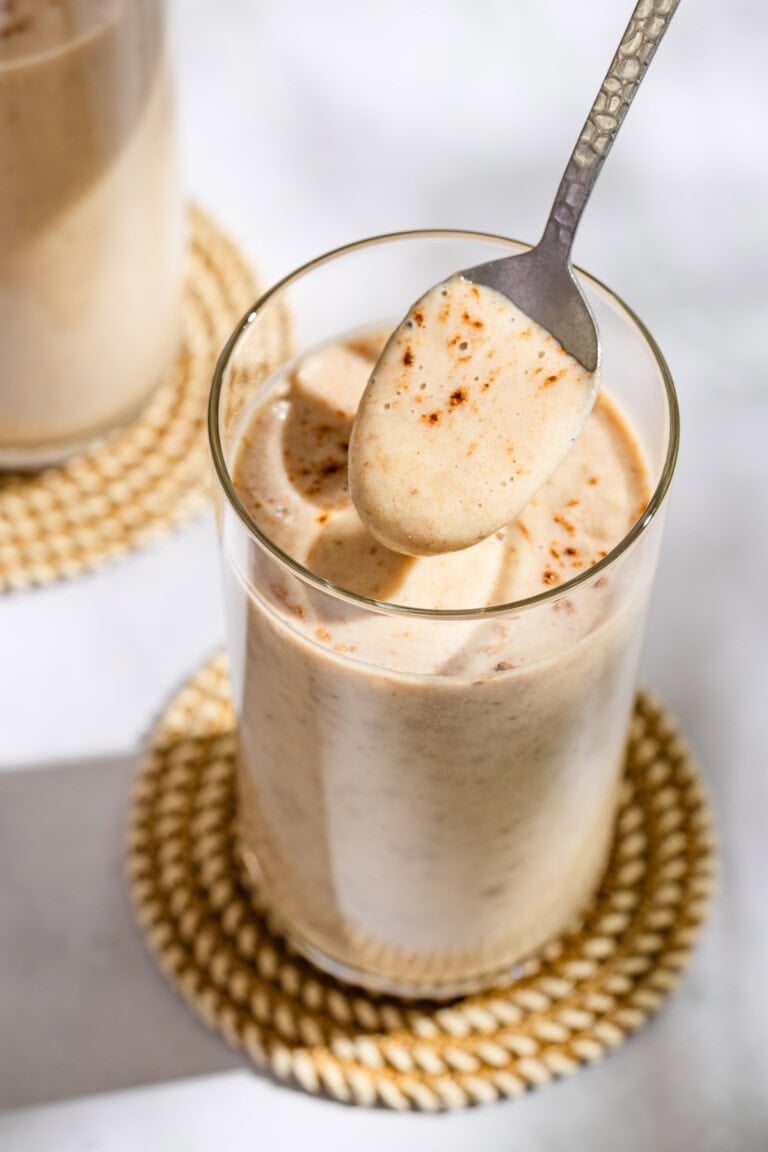 A spoonful of the date shake being held above a glass with the rest of the shake on a coaster.