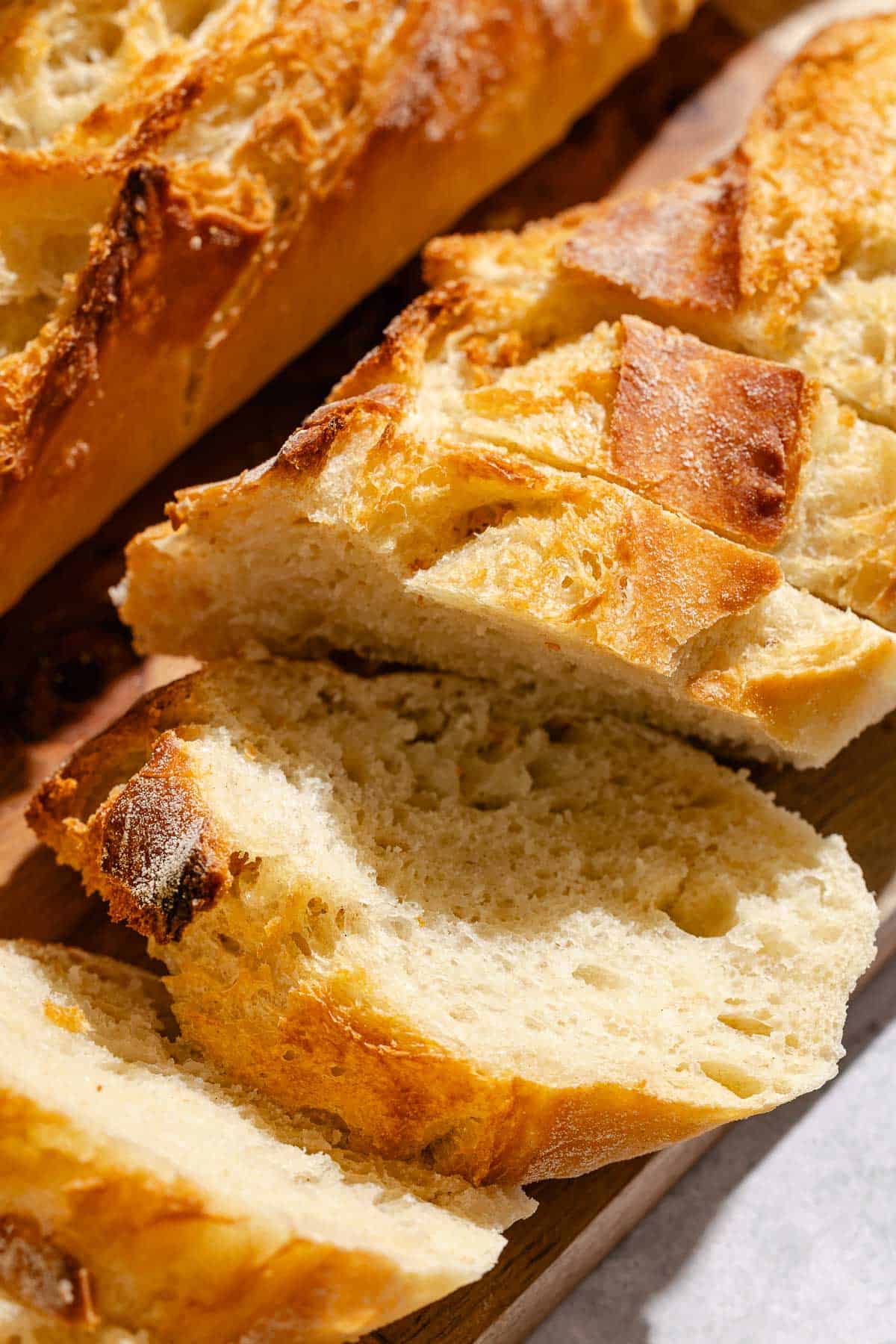 A close up of a sliced baked baguette on a wooden serving board.